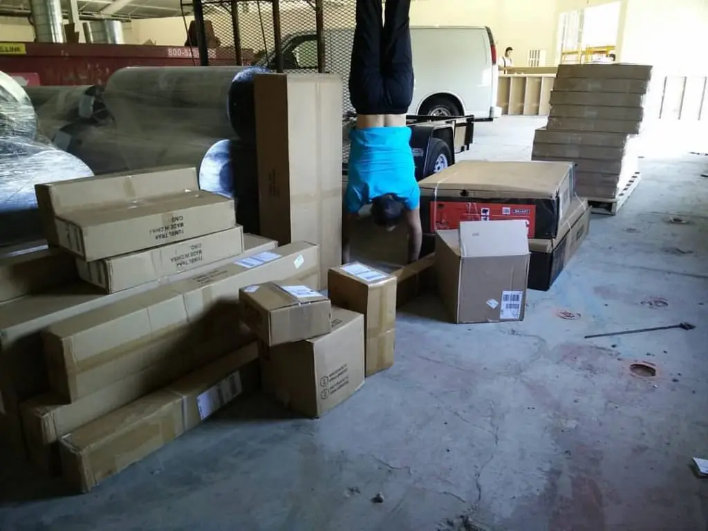 Person in a blue shirt doing a handstand next to cardboard boxes.