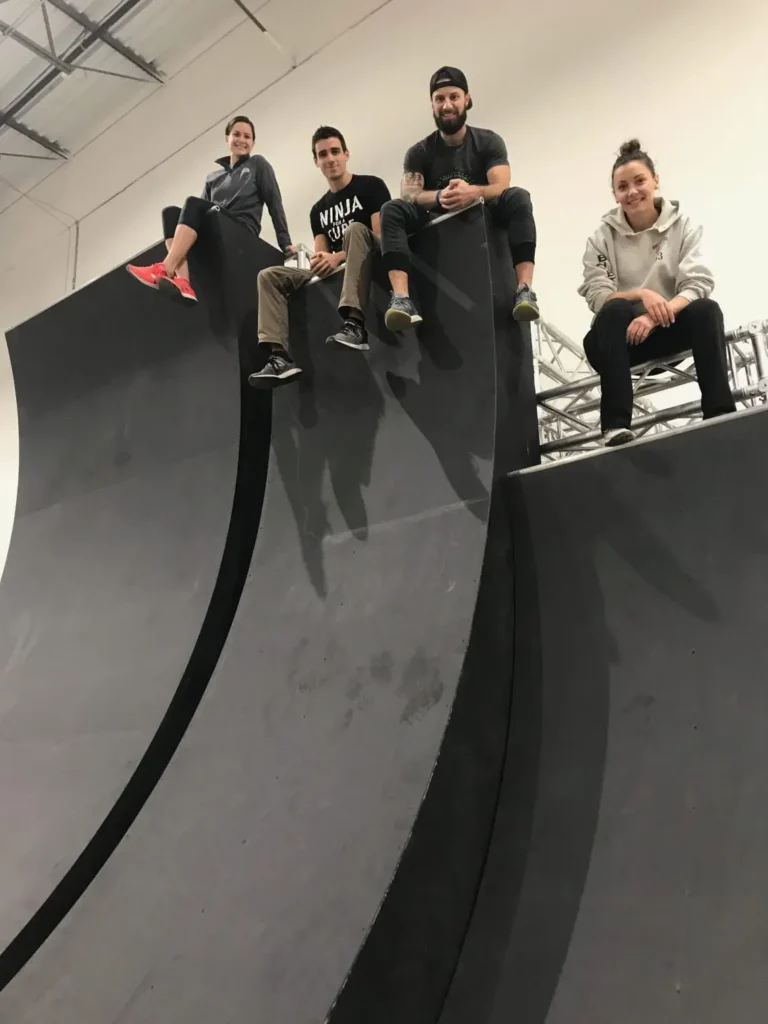 Four adults sit atop a dark grey Warped Wall, looking down at the camera.