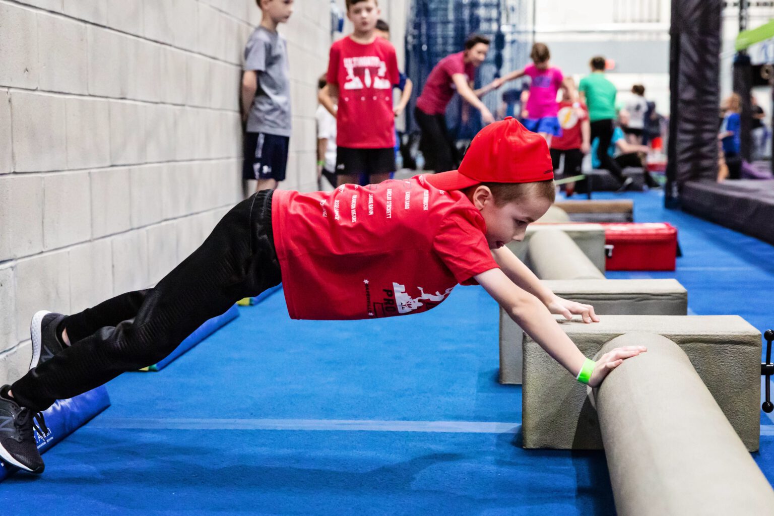 Boy in red shirt doing an incline push-up on staggered half logs.