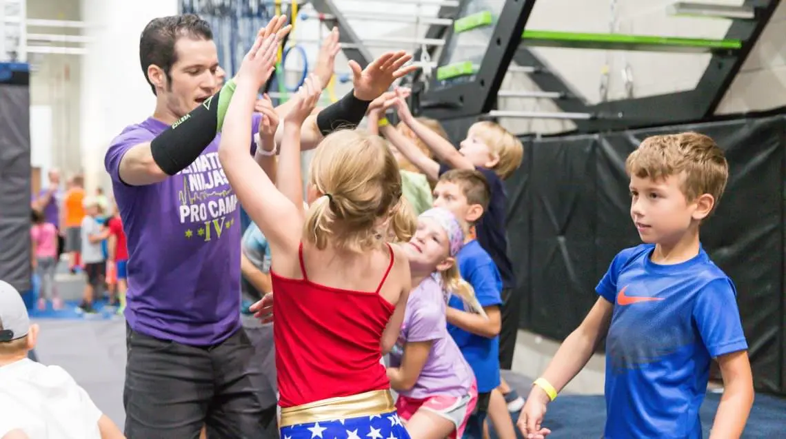 Kids and an Ultimate Ninjas coach in a purple shirt high-fiving in a group circle.