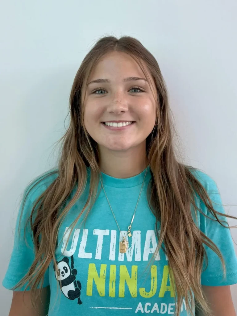 Smiling girl with long brown hair wearing an Ultimate Ninjas teal t-shirt.